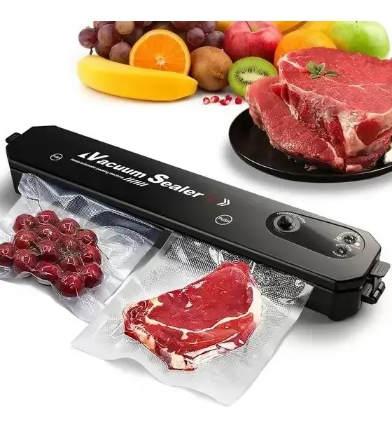 Dispositivo de sellado al vacío negro en funcionamiento, con bolsas de carne y uvas siendo selladas, rodeado de frutas frescas y carnes crudas en el fondo.