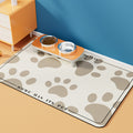 Tapete antideslizante e impermeable beige con huellas para comedero de mascotas.
